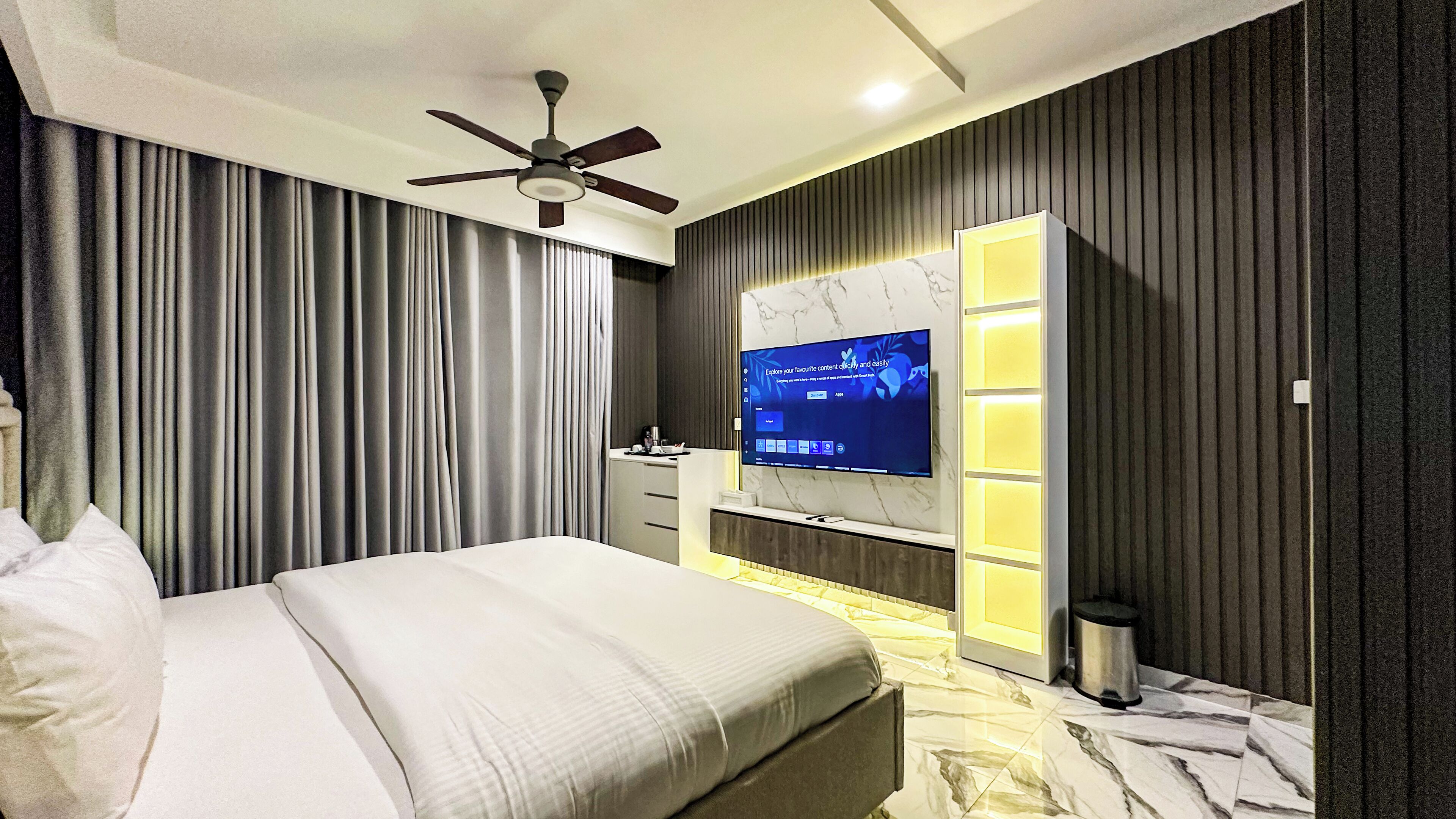 A modern bedroom with a bed, a ceiling fan, a TV mounted on a wall, and a bedside table.
