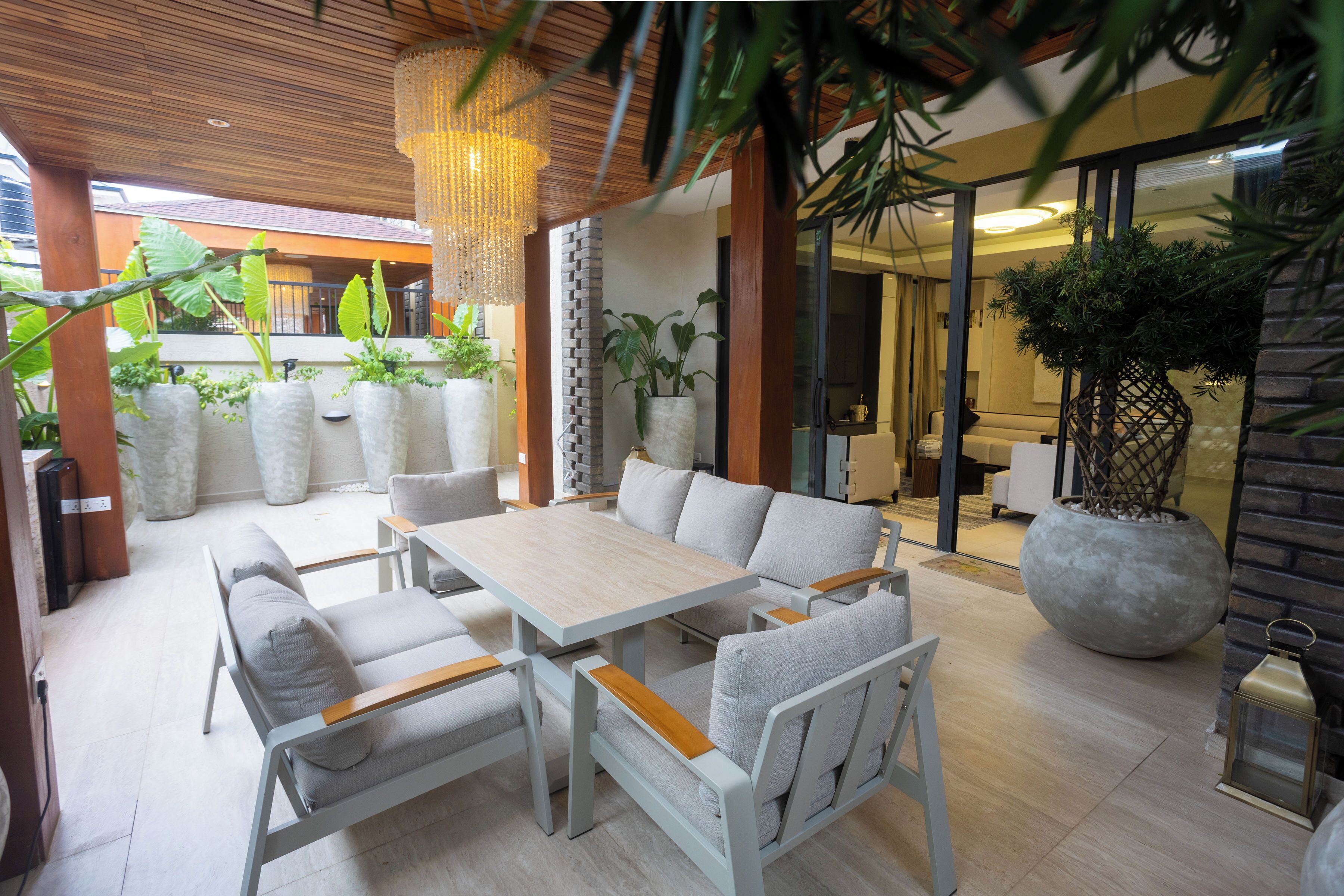 A modern outdoor seating area with a table and chairs, surrounded by potted plants and a hanging light fixture.