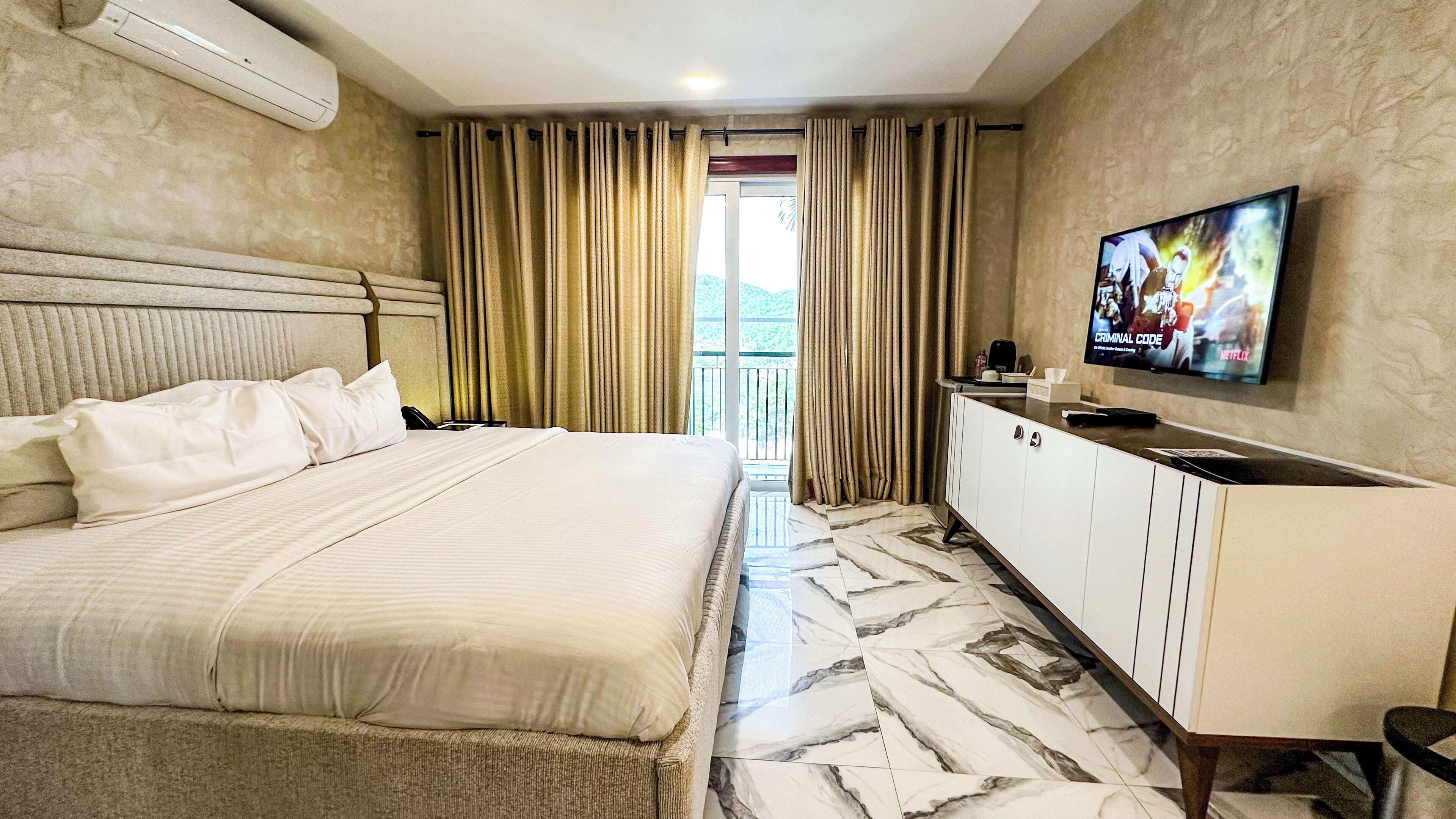 A hotel room with a bed, a TV, a desk, and a view of the outdoors.