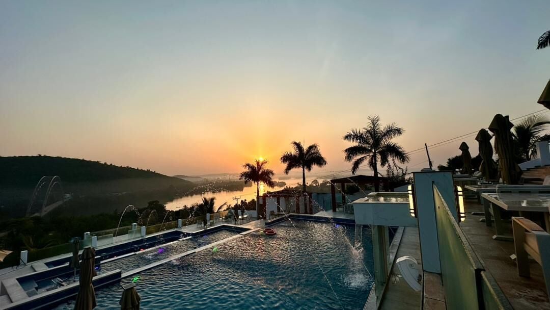 Ein Poolbereich mit Sonnenuntergangsblick, Palmen und einer entfernten Landschaft.