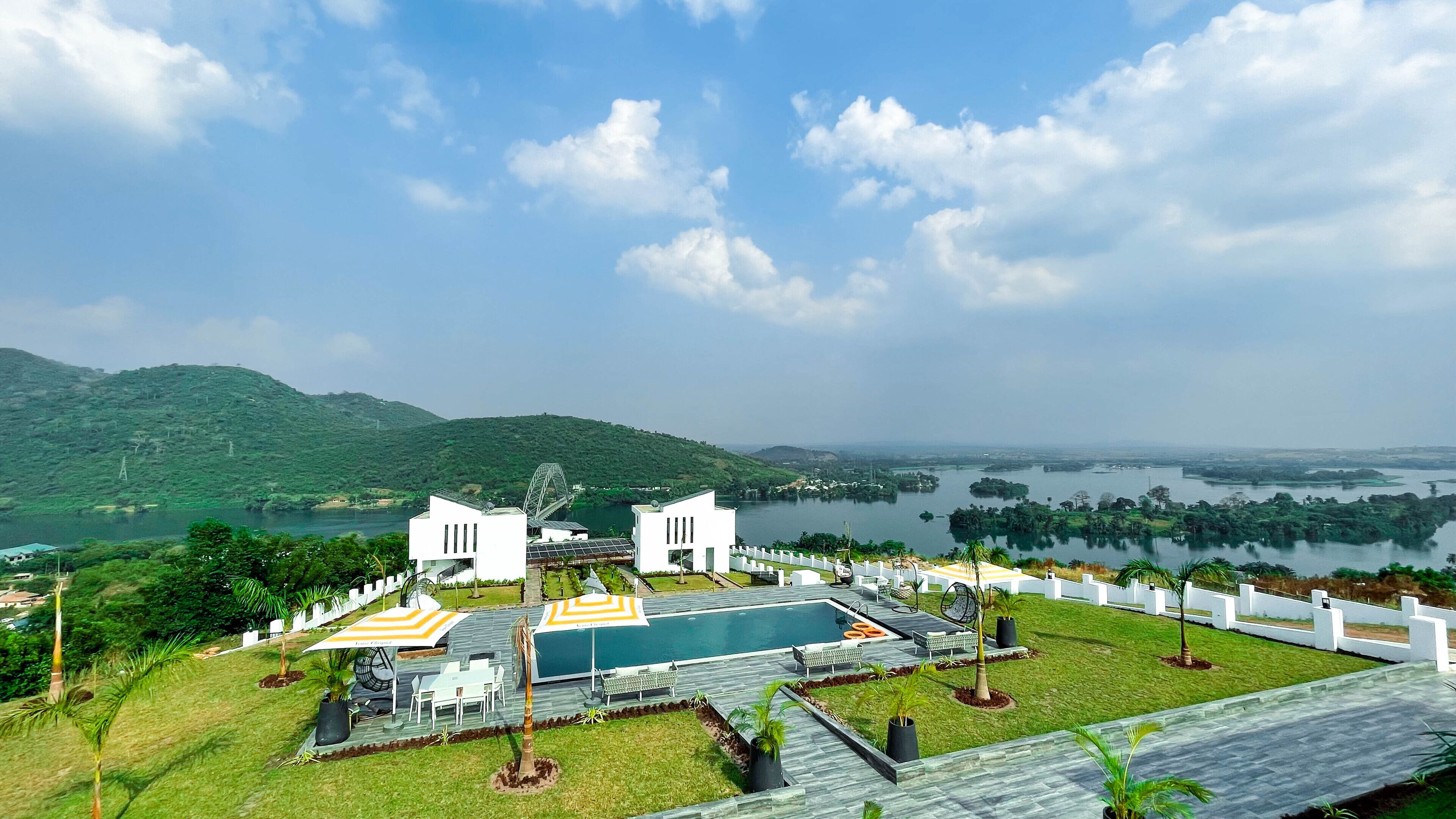 Un resort con piscina, mobiliario exterior y vistas a un lago y colinas.