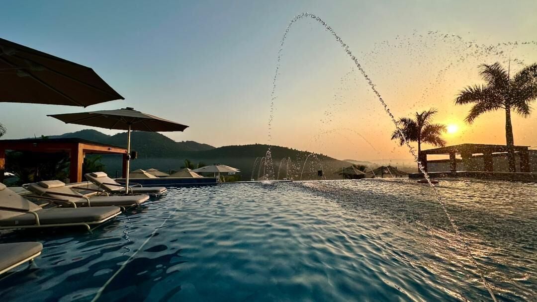 A pool area with lounge chairs and umbrellas, a water feature, and a sunset view.