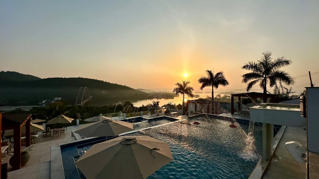 A swimming pool with a sunset view, palm trees, and a bridge in the background.