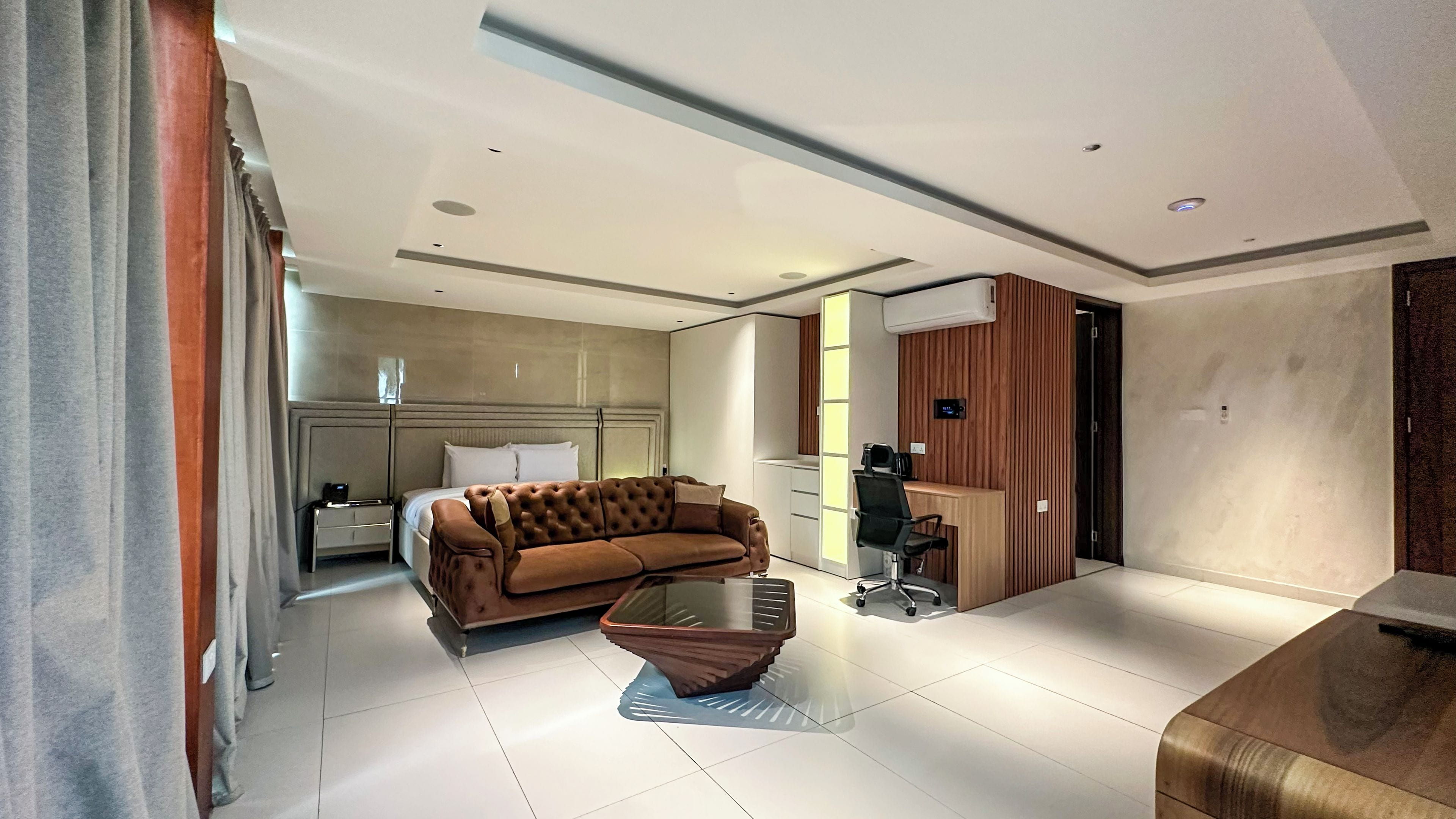 Une chambre d’hôtel moderne équipée d’un canapé, d’une table basse en verre, d’un bureau avec une chaise et d’un lit avec une tête de lit.