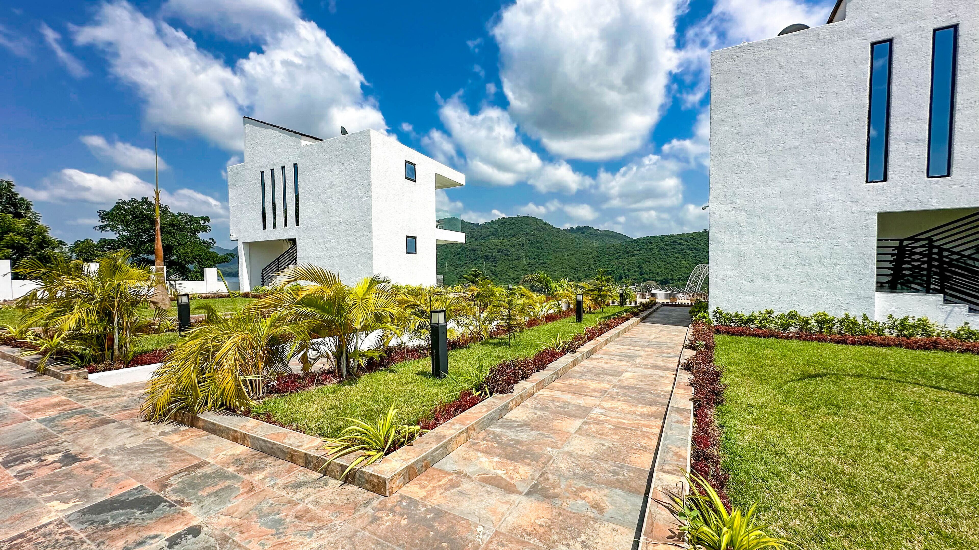 Un bâtiment moderne avec un chemin pavé, entouré d’une végétation bien entretenue et sous un ciel dégagé.