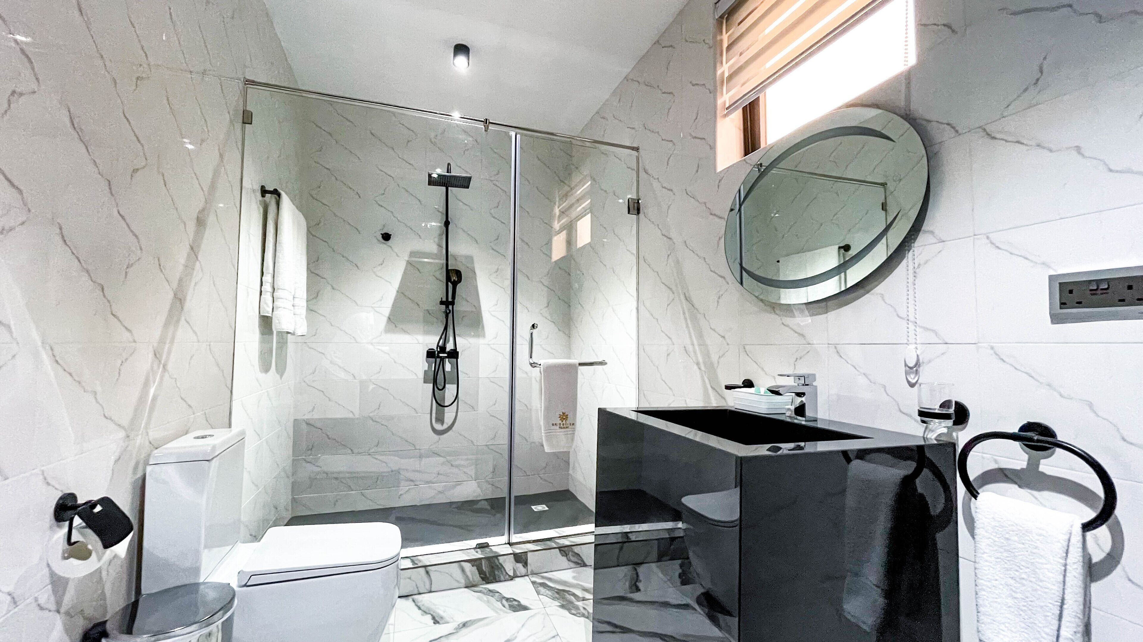 A modern bathroom with a glass-enclosed shower, a standalone sink, and a round mirror.