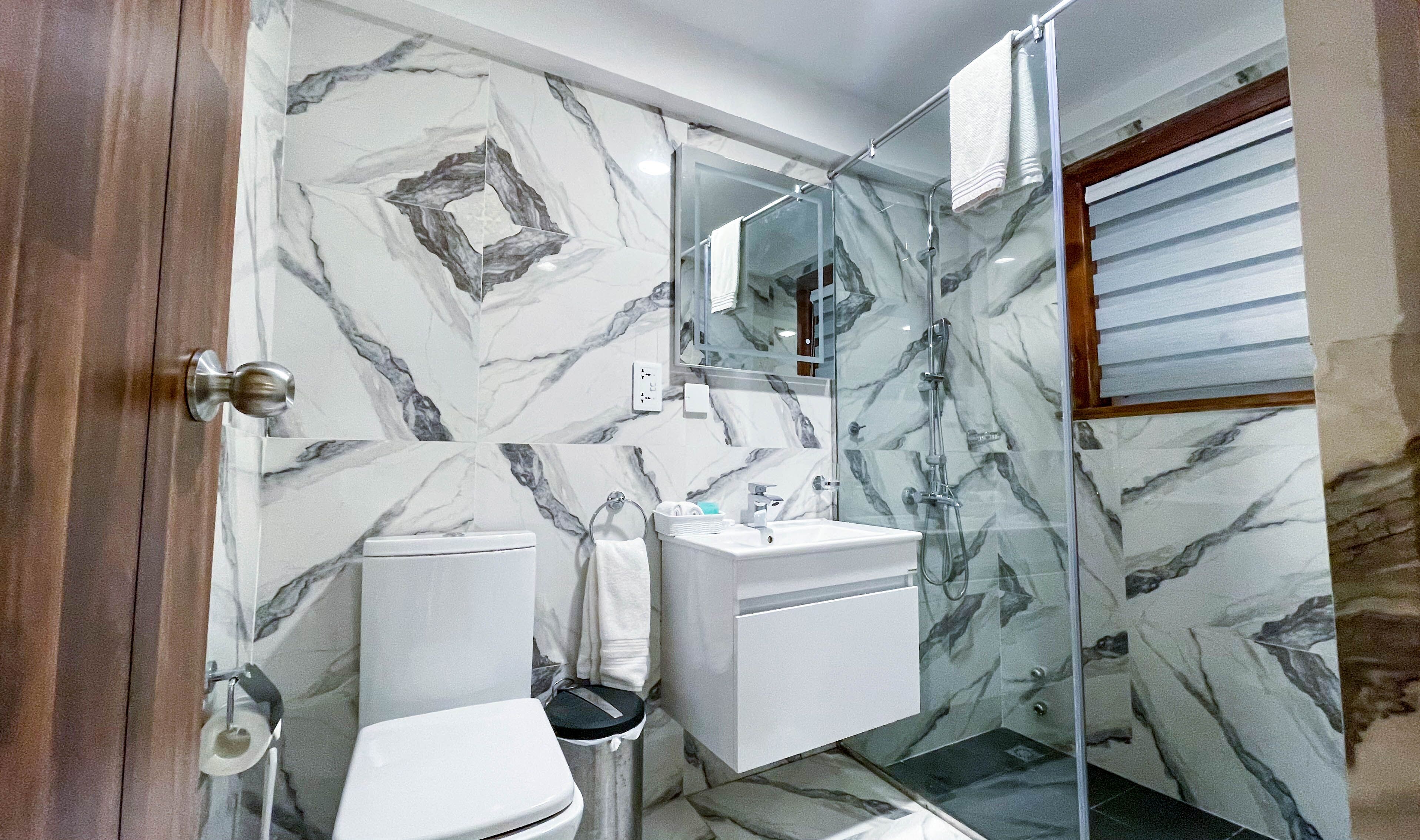 A bathroom with marble walls, a glass shower enclosure, a toilet, and a sink.