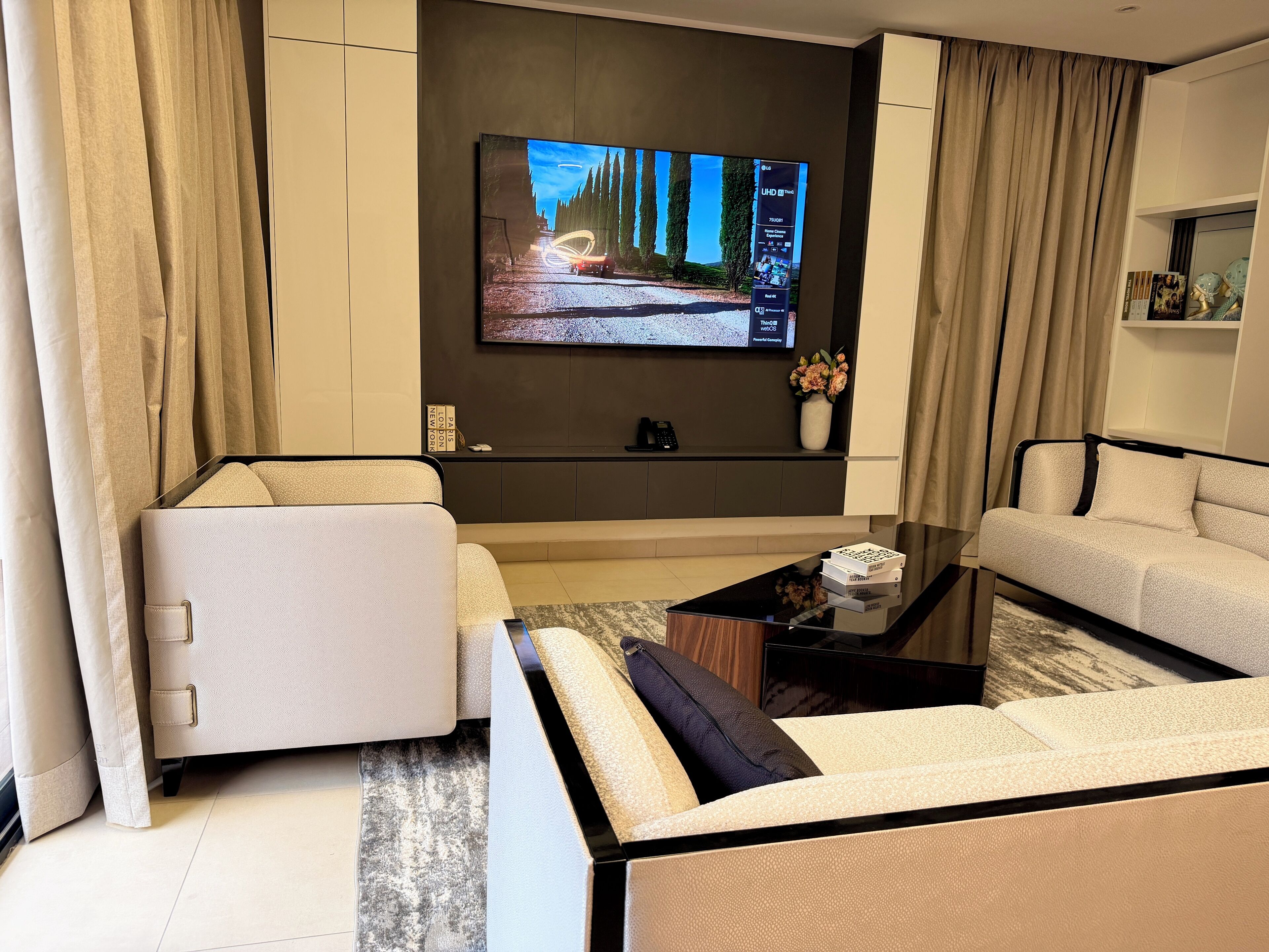 A modern living room with a flat-screen TV mounted on the wall, a sofa, a coffee table, and a side table with a vase of flowers.