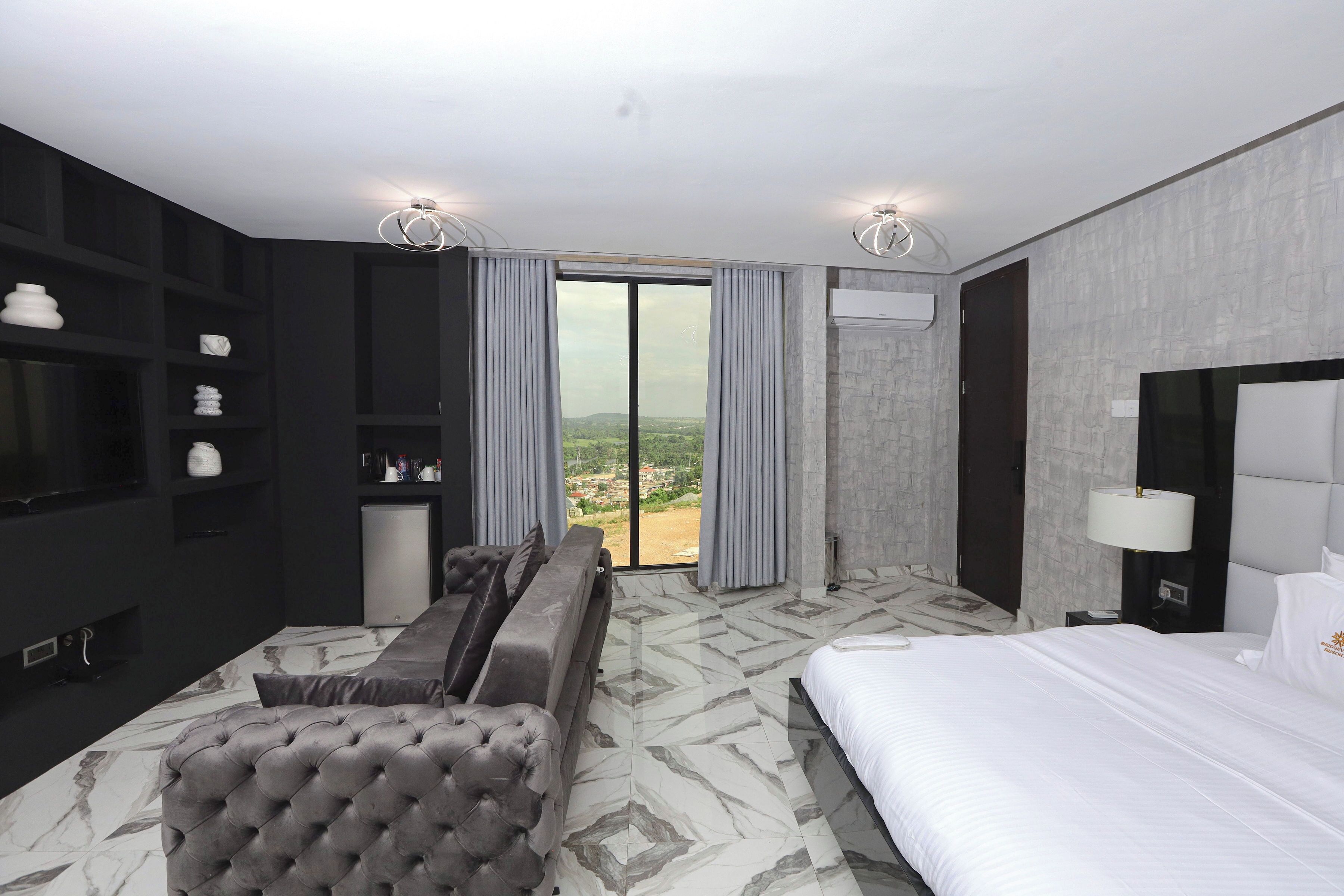 Una habitación de hotel moderna con una cama grande, un sofá, un televisor y vistas al exterior.
