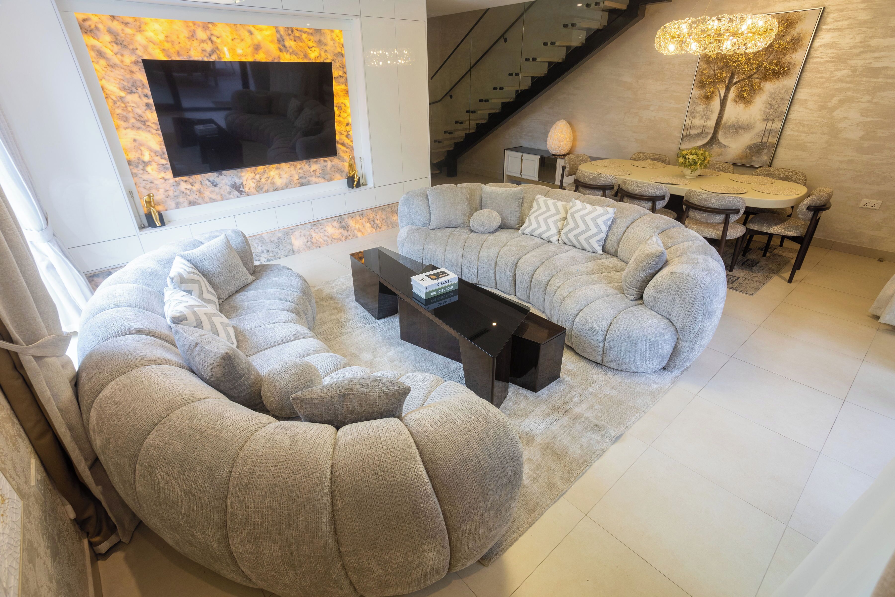 A modern living room with a curved sectional sofa, a glass coffee table, and a dining area with a table and chairs.