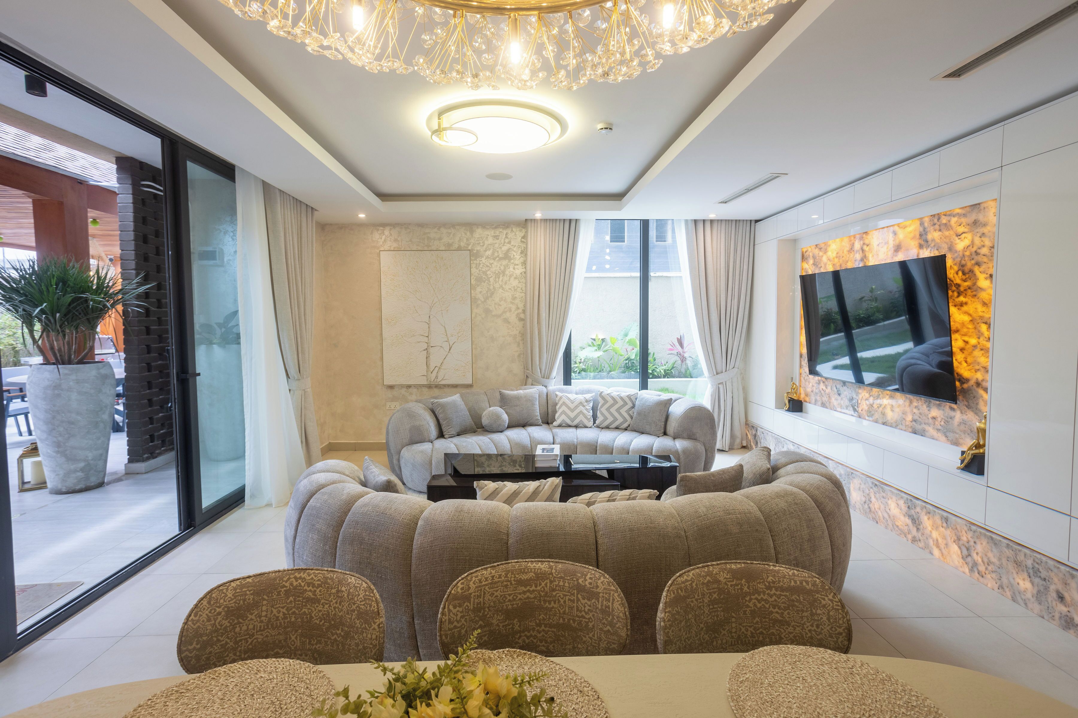A modern living room with a sectional sofa, a dining table with chairs, a large TV, and a decorative chandelier.