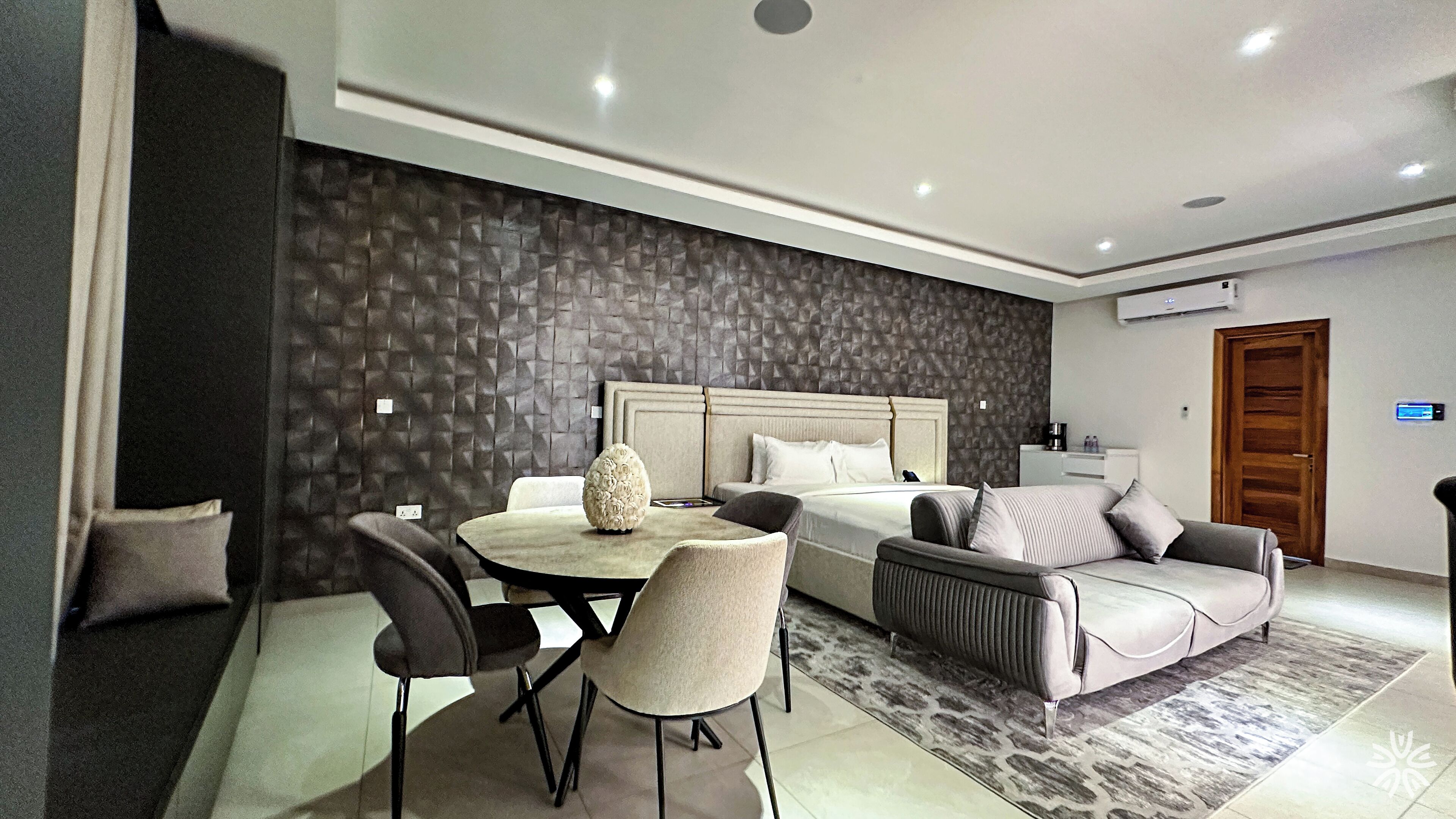 Een moderne hotelkamer met een groot bed, een eettafel met stoelen, een bank en een kamer met een patroon op de muur.