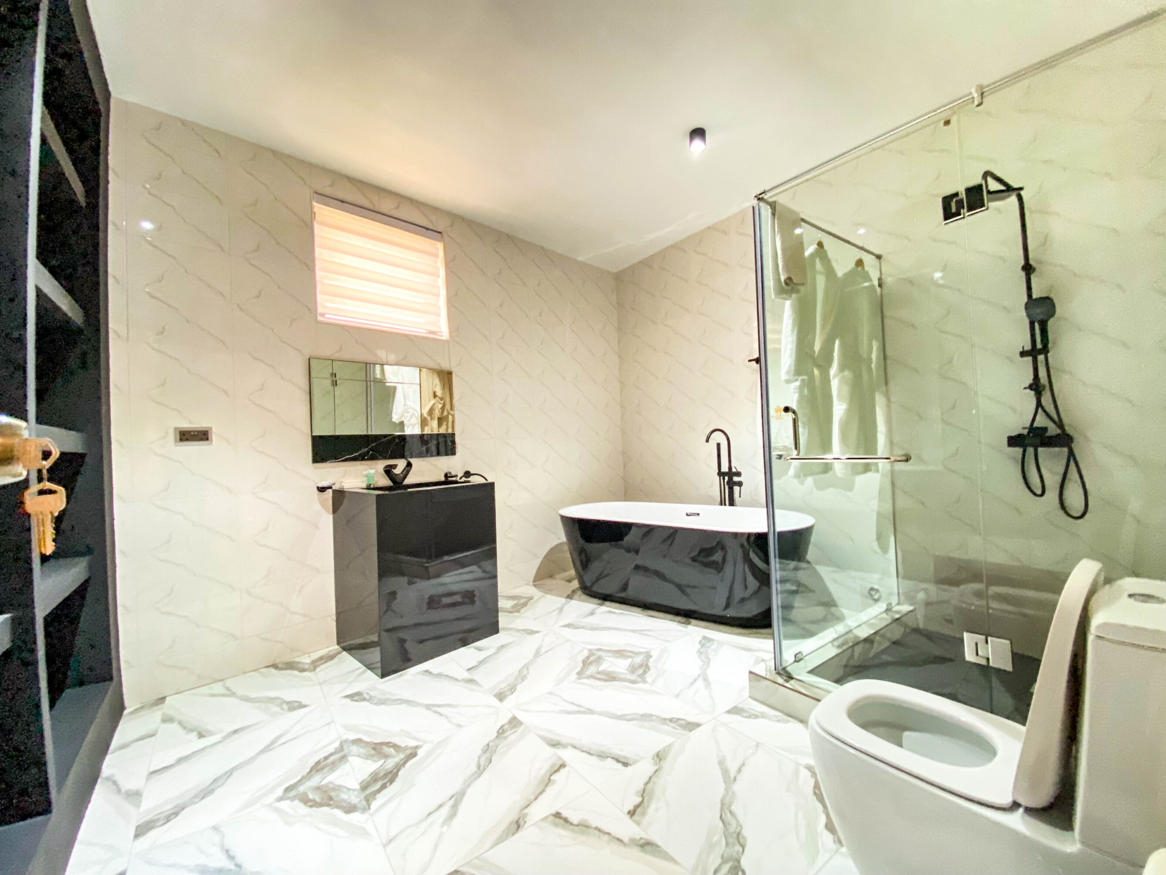 A modern bathroom with a marble floor, a freestanding bathtub, a glass-enclosed shower, and a toilet.