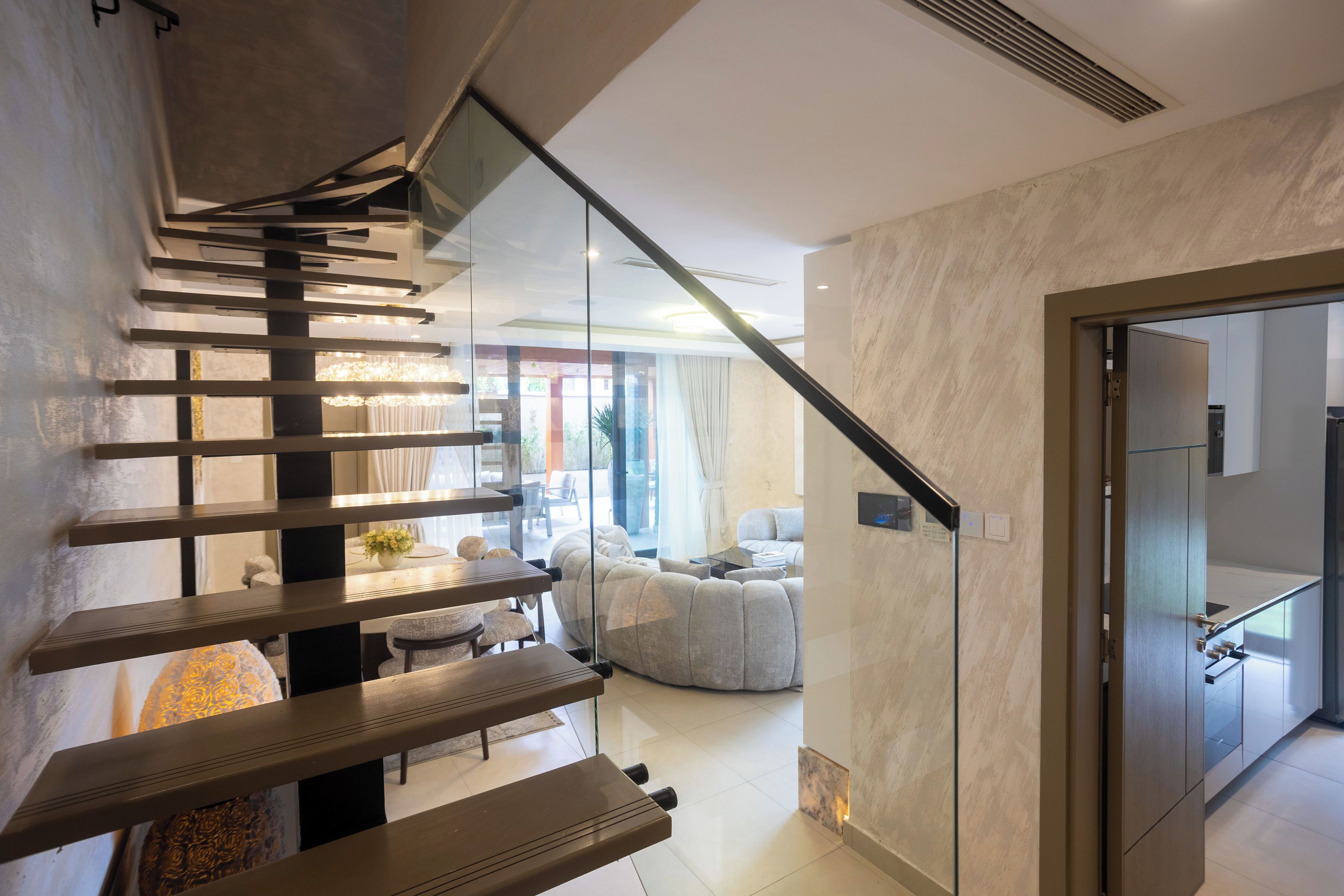Un interior moderno con una escalera, un área de descanso con sofá y sillones, y un separador de vidrio.