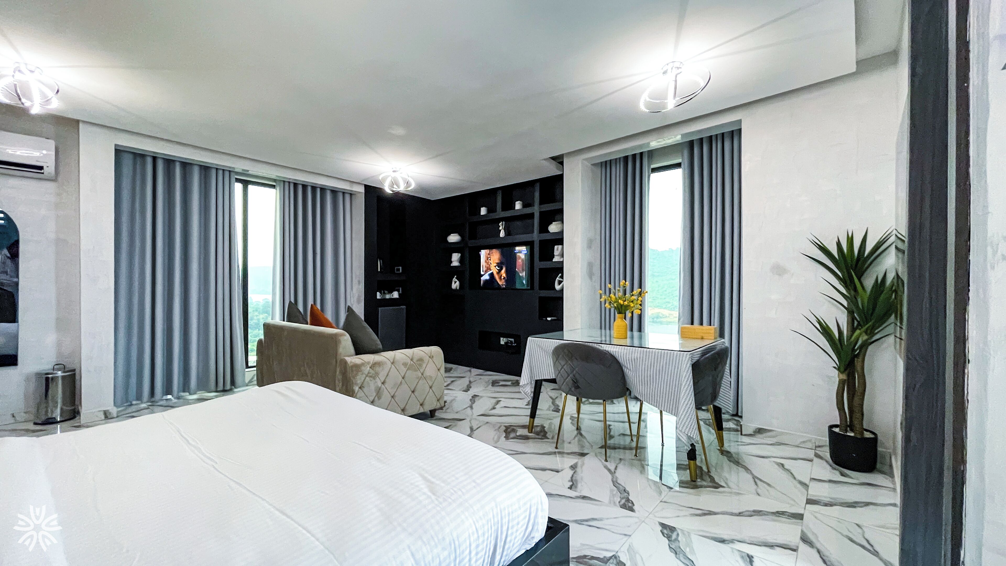 A modern hotel room with a large bed, a desk with a chair, a television, and a potted plant.