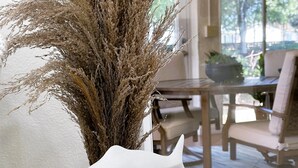 Una habitación con un sofá blanco texturizado, una mesa de comedor de madera con sillas y un jarrón con plumas de plumas de pampa secas.