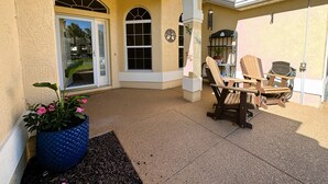 Un patio techado con dos sillas de madera, una planta en maceta y una puerta que da al interior.