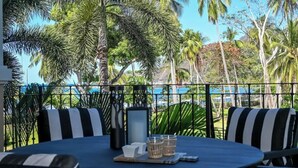 Ein Balkon mit Tisch, Stühlen und Blick auf Palmen und ein Schwimmbad.