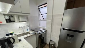 A compact kitchen with white cabinets, a stainless steel stove, a refrigerator, and a window with a view. - Beautiful apartment with excellent location (Buenos Aires)