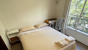 A bedroom with a bed, a desk, a chair, and a window with a view of greenery. - Beautiful apartment with excellent location (Buenos Aires)