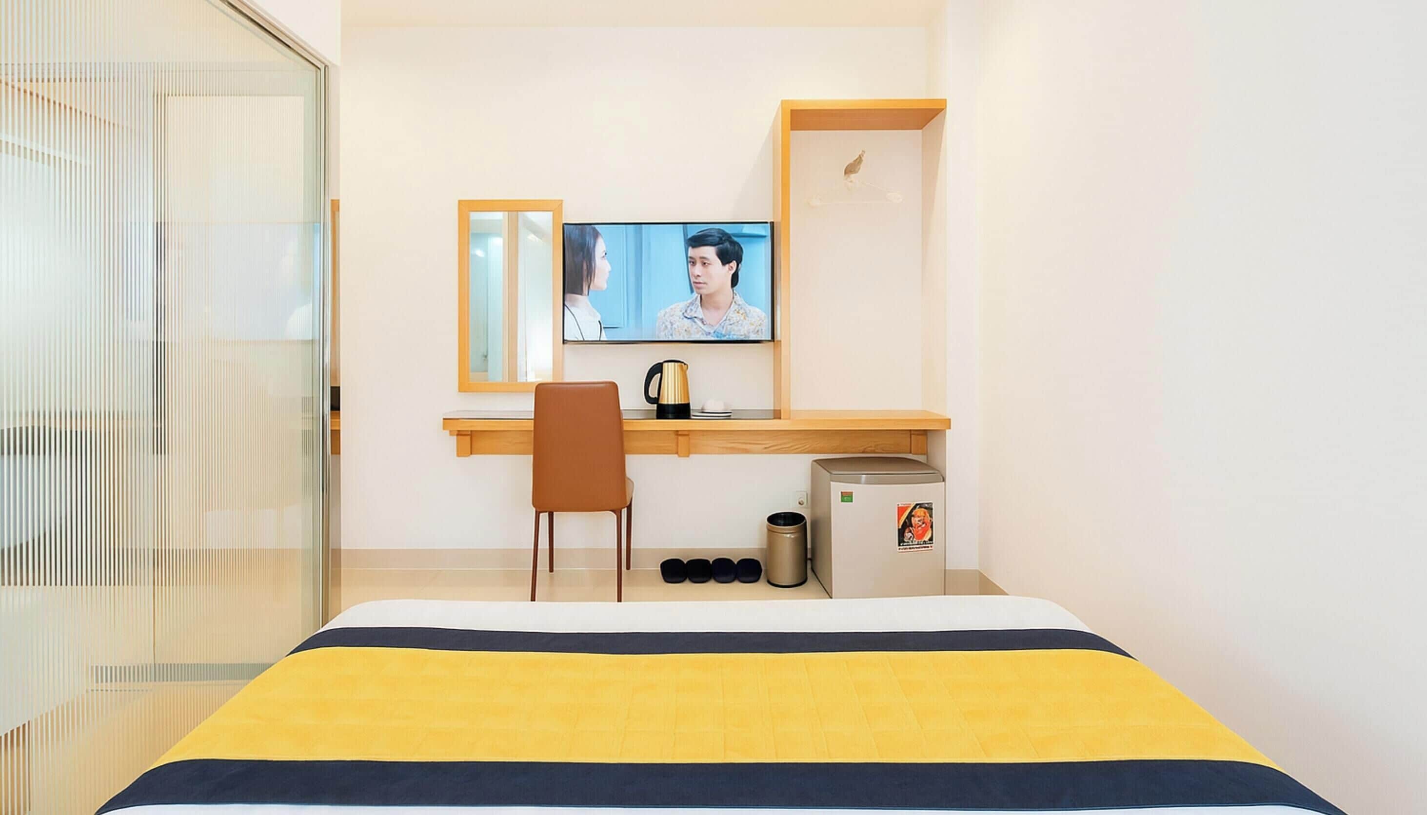 Een hotelkamer met een bed, bureau, stoel, televisie, koffiezetapparaat en een prullenbak.