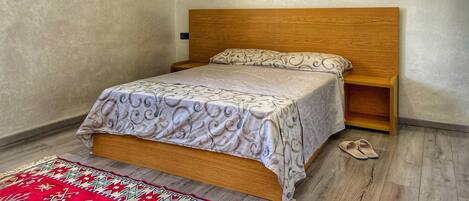 Un dormitorio con cama de madera, colcha estampada, alfombra roja y beige, y un cuadro de paraguas en la pared.