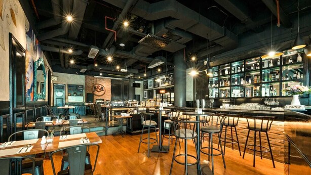 A restaurant with a bar area, wooden tables, and bar stools. - MaxOneHotels Premier Melawai (Jakarta)