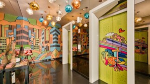 A brightly lit corridor with colorful murals, hanging spherical lights, and a green wall with a cartoonish design. - MaxOneHotels Premier Melawai (Jakarta)