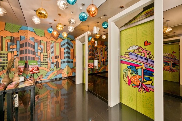 A brightly lit corridor with colorful murals, hanging spherical lights, and a green wall with a cartoonish design. - MaxOneHotels Premier Melawai (Jakarta)