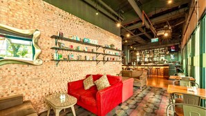 A cozy lounge area with a red sofa, a small table, and a brick wall with bookshelves. - MaxOneHotels Premier Melawai (Jakarta)