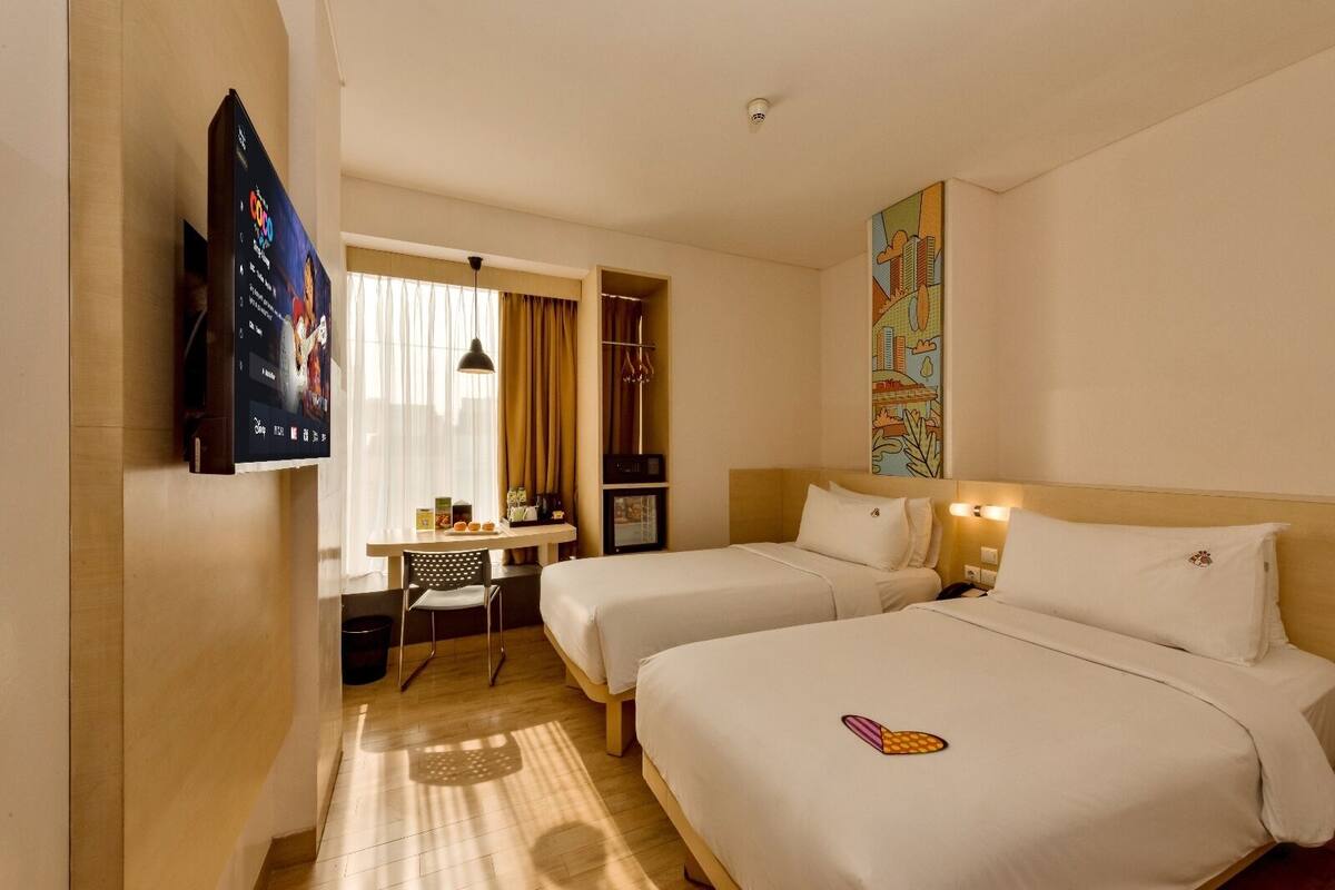 A hotel room with two beds, a desk, a TV, and a painting on the wall.