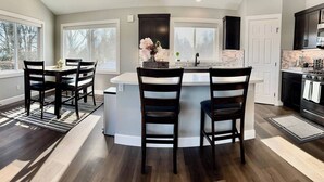 Een moderne keuken met een centraal eiland, donkerhouten stoelen en uitzicht op de omgeving door grote ramen.