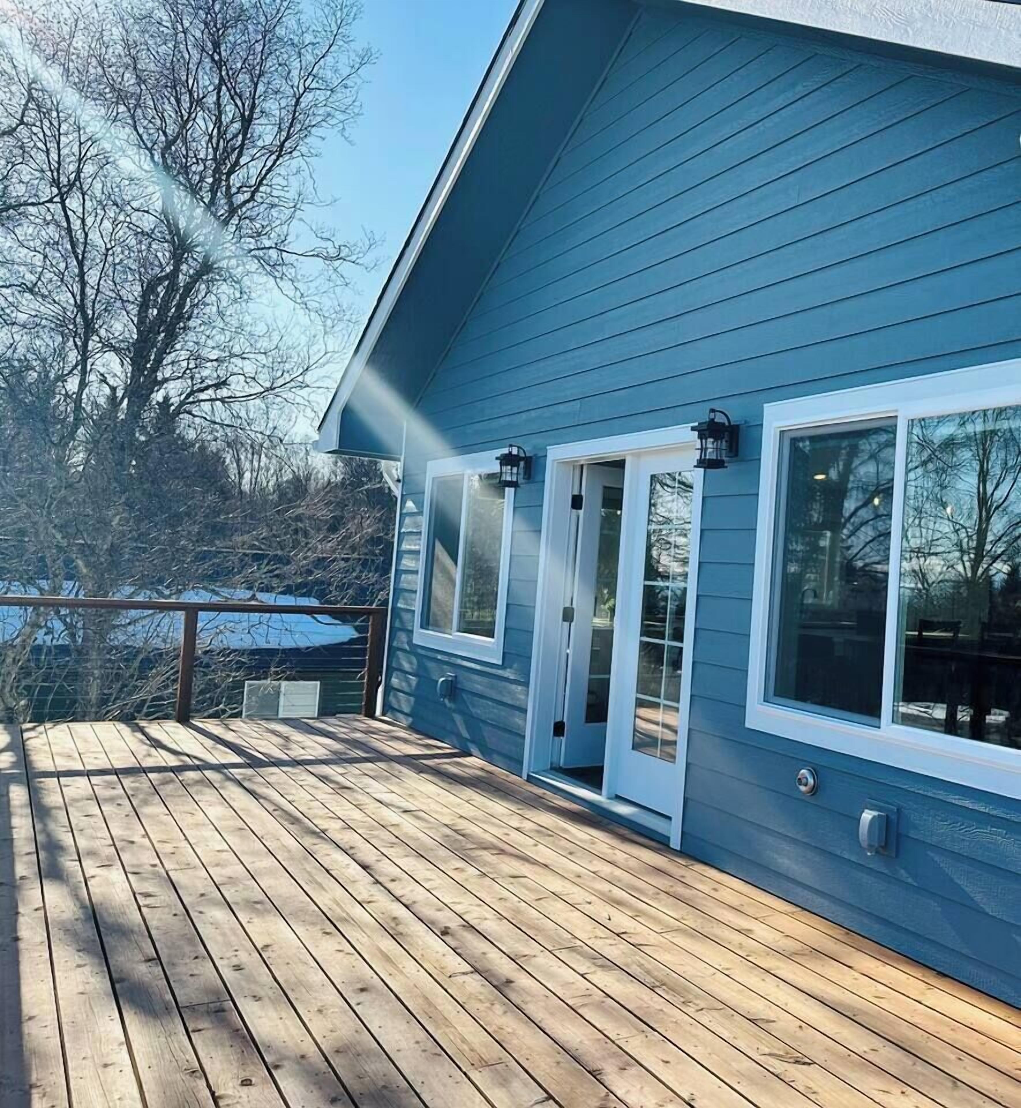 A blue house with a wooden deck, a glass door, and a window.