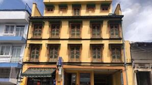 Un hôtel à plusieurs étages, avec une façade jaune, des balcons dotés de rampes vertes et un restaurant situé au rez-de-chaussée.