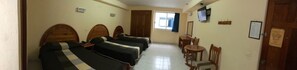A hotel room with four beds, a desk, chairs, a window, and a TV.