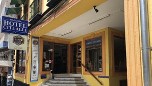 L’entrée d’un hôtel, avec un escalier menant à la porte, une enseigne indiquant « Hôtel Citalli » et une autre indiquant « Jarr Cafe ».