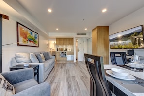 Una sala de estar moderna con un sofá, una mesa de comedor para dos personas y una cocina al fondo.
