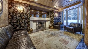 A cozy living room with a fireplace, leather sofas, and a large window offering a view of the outdoors. - Le Chamois 211 - Ski in Ski out, Common Pool, Hot Tub & Gym (Whistler)