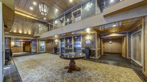 A spacious lobby with a central round table, multiple elevators, and a high ceiling with wooden beams. - Le Chamois 211 - Ski in Ski out, Common Pool, Hot Tub & Gym (Whistler)