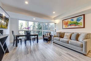 A modern living room with a large window, a dining area, and a sofa.
