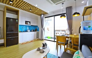 A modern kitchen with white cabinets, a black refrigerator, and a blue backsplash. There is a dining area with a table, chairs, and a water dispenser. - Friendly House QMP - D'Capitale (Hanoi)