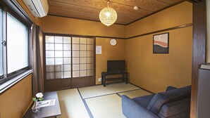 Perinteinen japanilainen huone, jossa on tatamimatto, sohva, pieni pöytä maljakolla, televisio ja liukuovi.