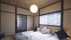 Perinteiseen japanilaiseen tyyliin sisustettu makuuhuone, jossa on kaksi sänkyä, shoji-liukuovi ja riippuvalaisin.