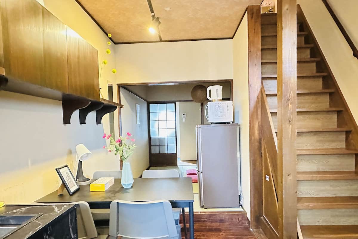 A kitchen with a dining area, wooden staircase, and a refrigerator.