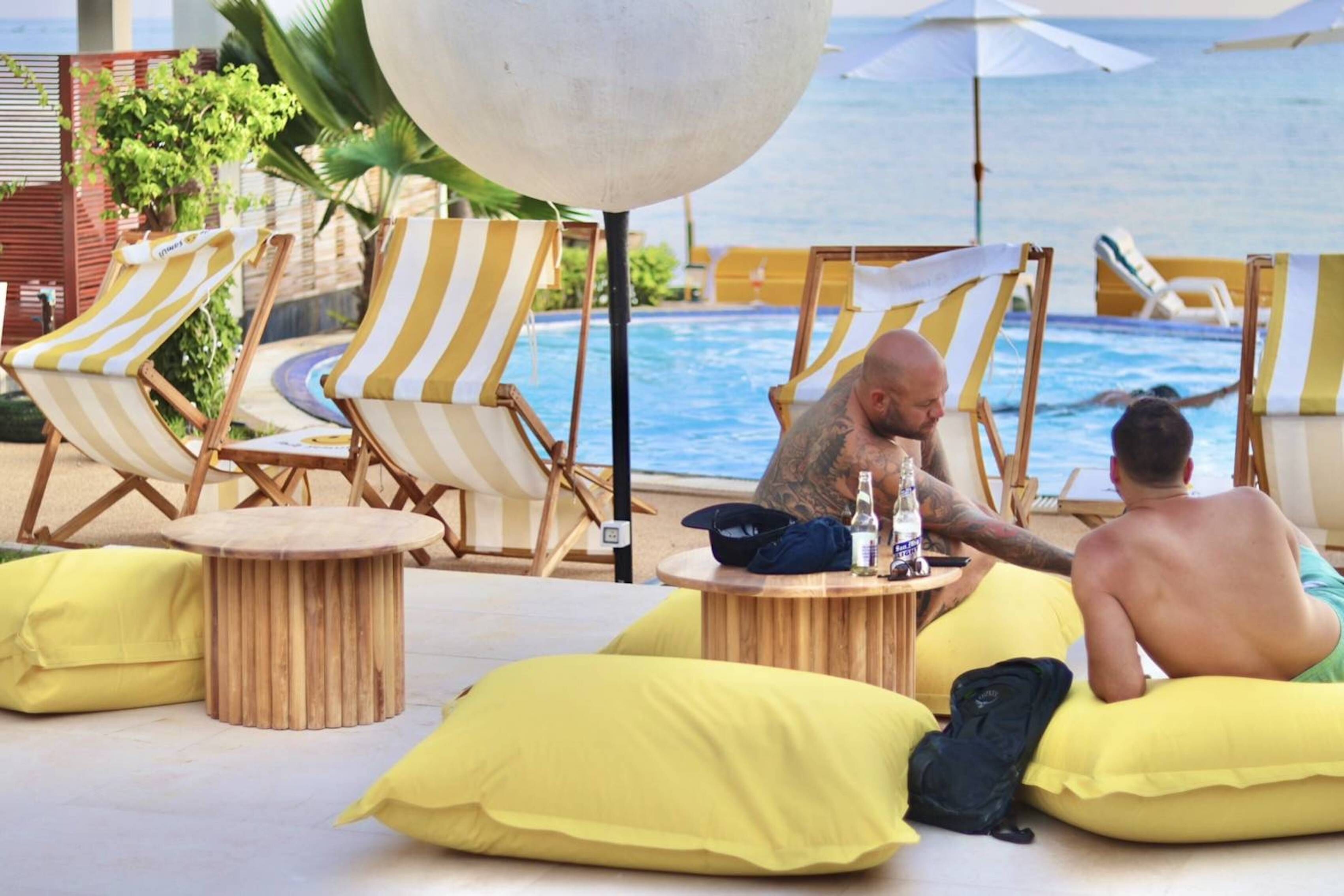 A poolside area with striped lounge chairs, yellow cushions, and a round wooden table.