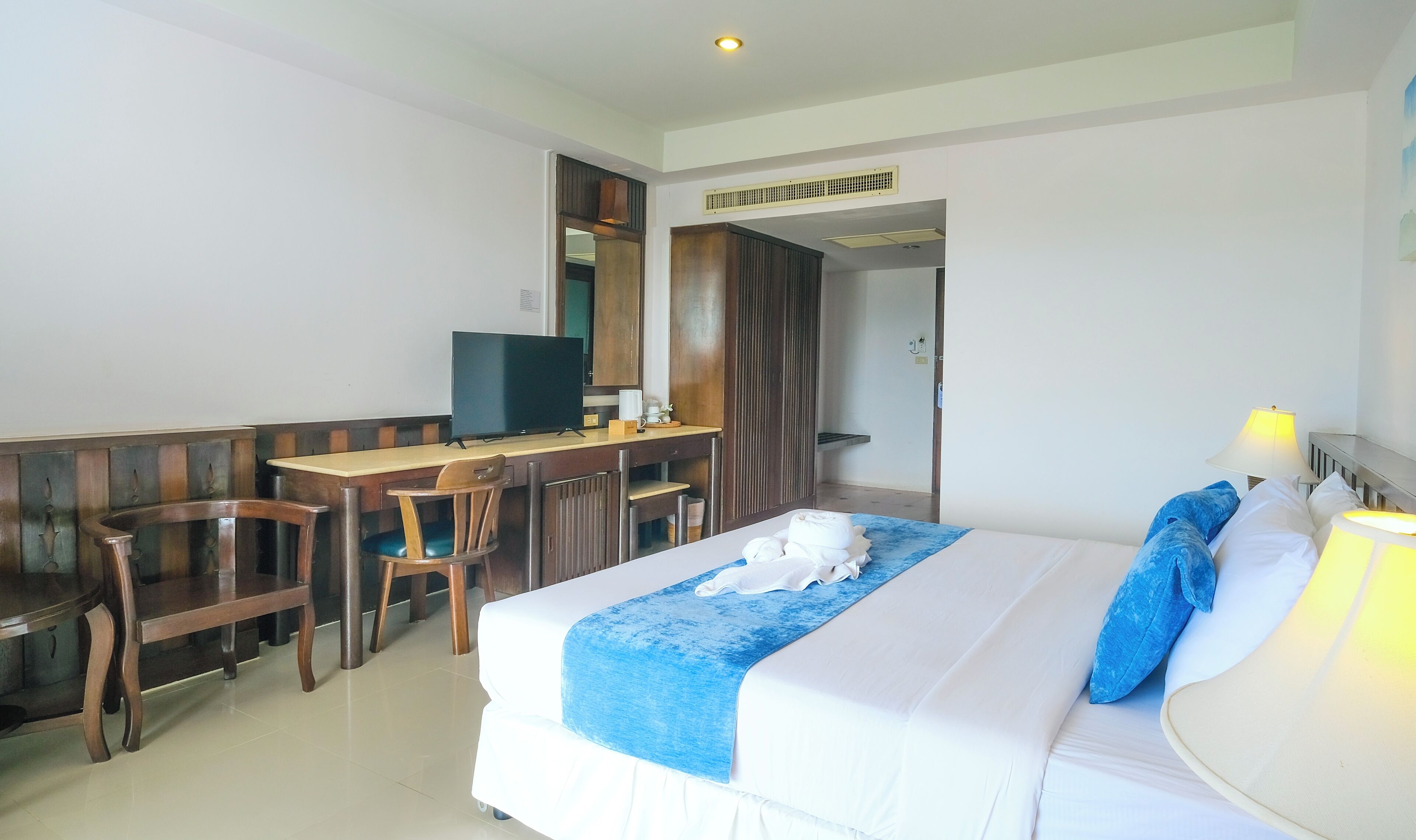Una habitación de hotel con cama, escritorio con televisor, una silla y la puerta del baño.