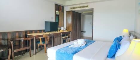 Una habitación de hotel con cama, escritorio con televisor, una silla y la puerta del baño.