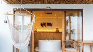 A modern bathroom with a large bathtub, a wooden chair, and a hanging hammock. - Smile Samui Chaweng Beach Front Resort (Koh Samui)