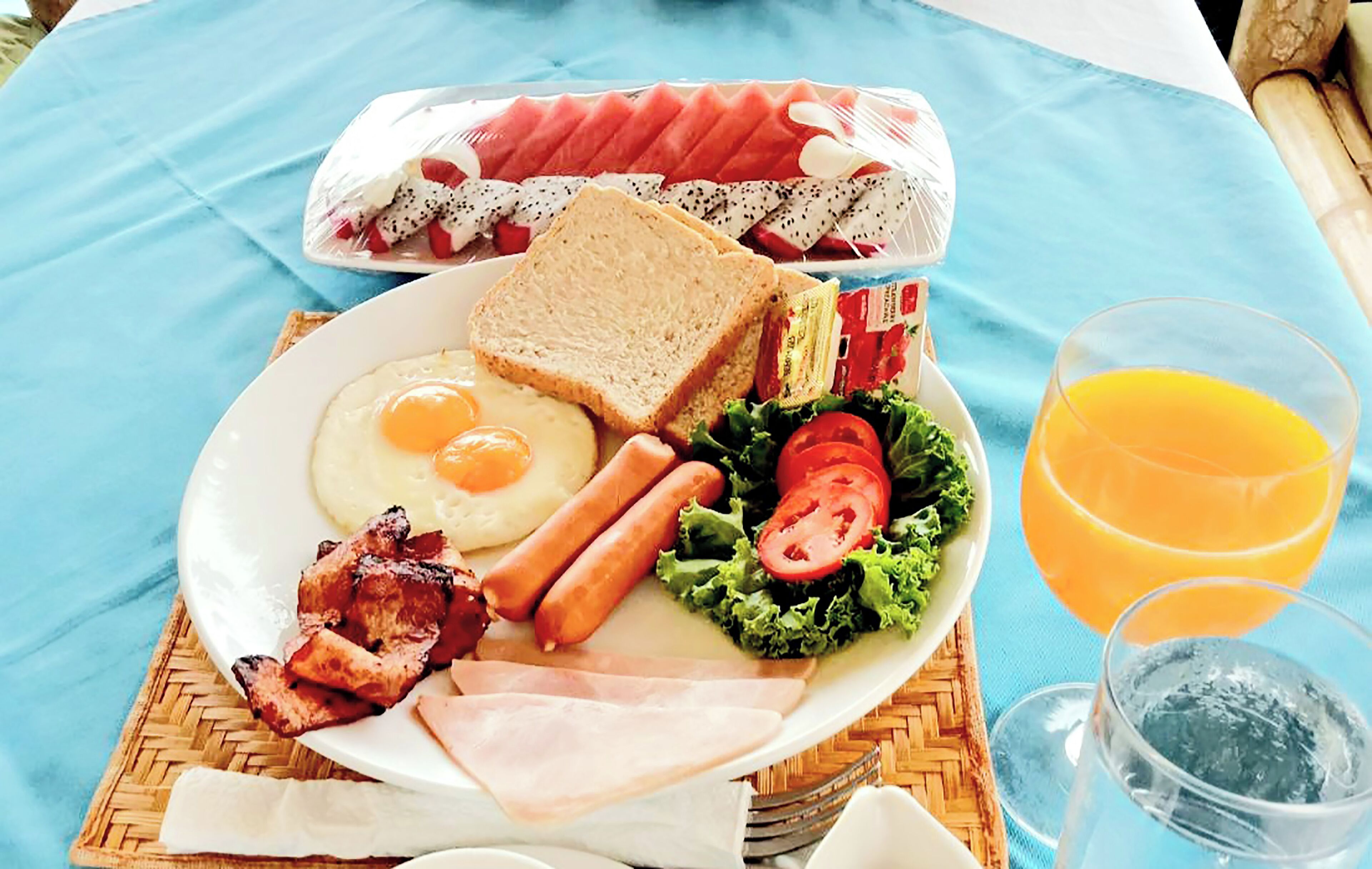 A breakfast plate with eggs, sausages, bacon, toast, tomatoes, lettuce, and a glass of orange juice.