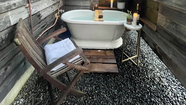 A rustic wooden cabin with a bathtub, a hanging chair, and a small table with candles. - Ocean Views, Beach Path, Private + Pickleball + Nature Baths (Grayland)